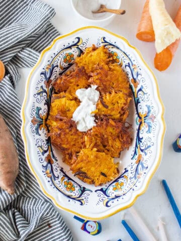 A batch of fried sweet potato latkes with carrot in a small serving bowl topped with a horseradish dip.