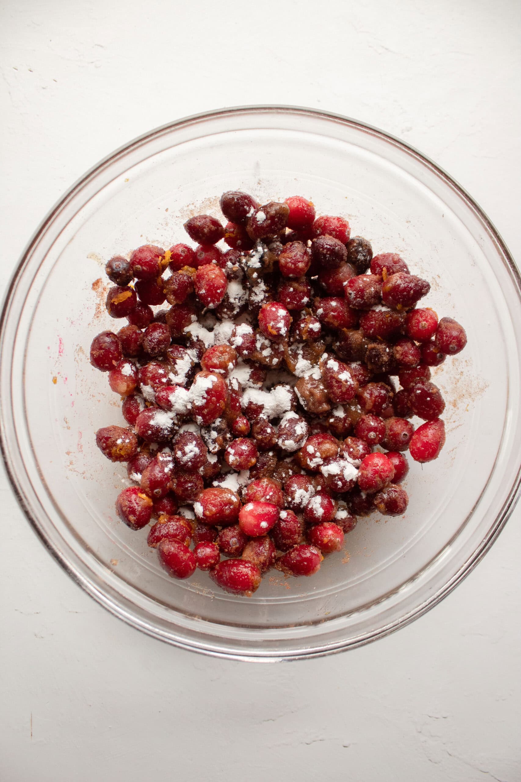 A large mixing bowl with fresh whole cranberries, sugar, orange juice, orange zest, cinnamon, and a pinch of cornstarch.