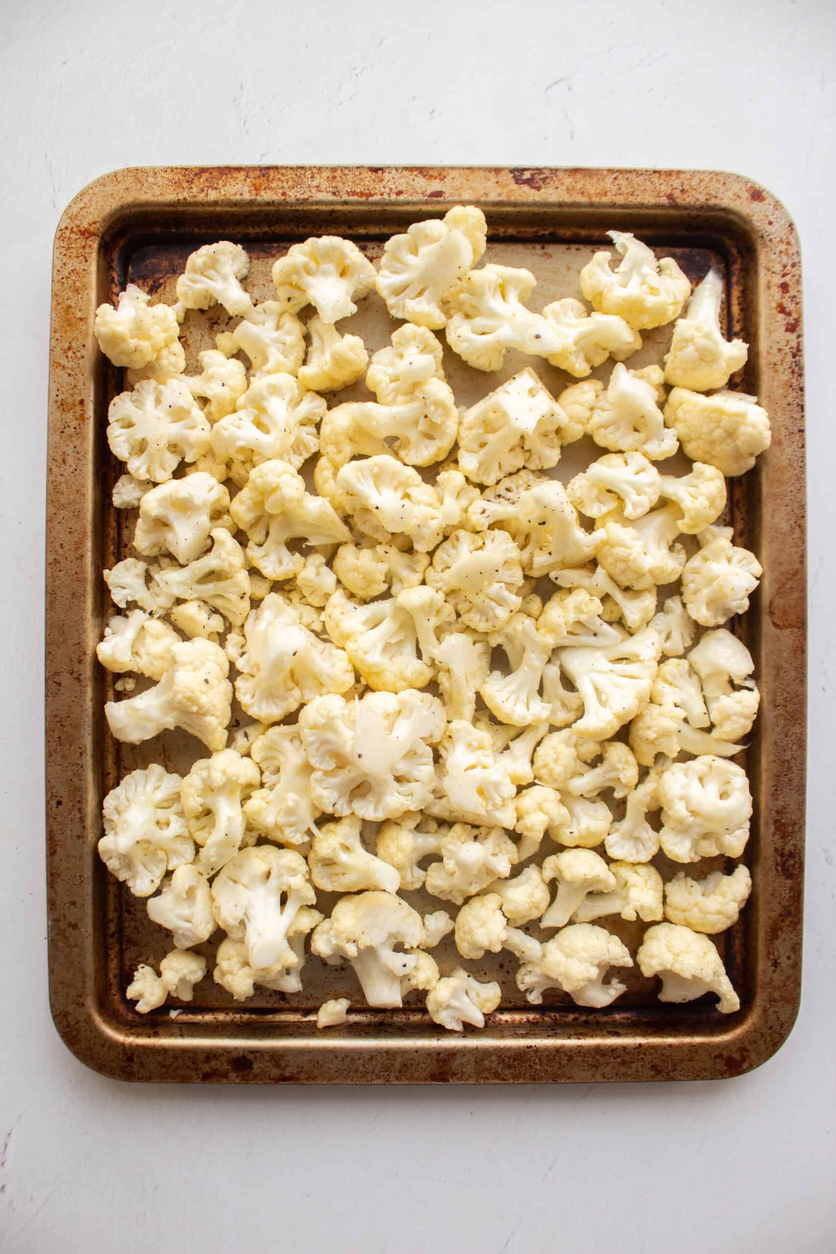 Chopped and seasoned cauliflower on a baking sheet before roasting.