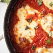 Close up of a piece of skillet chicken parmesan topped with basil.