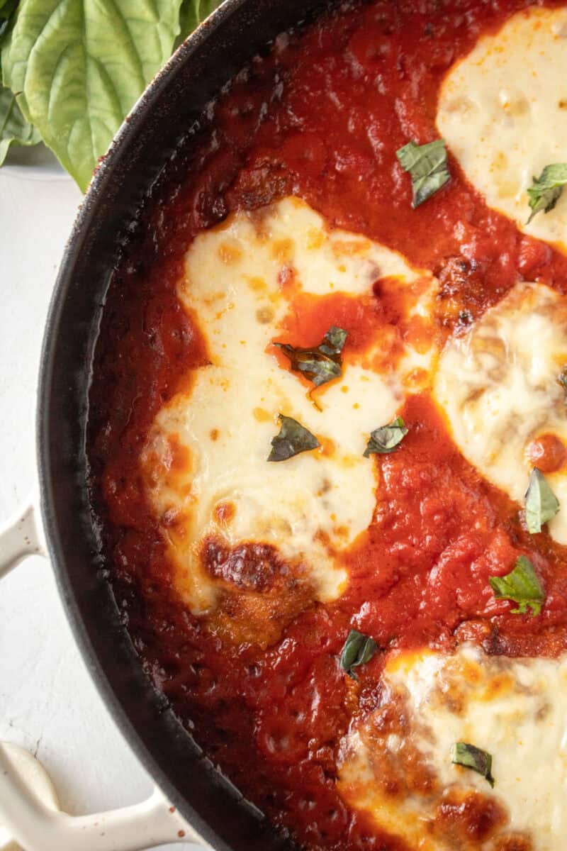 Close up of a piece of skillet chicken parmesan topped with basil.