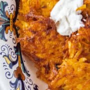 Close up of a sweet potato latke topped with horseradish dip in a serving bowl.
