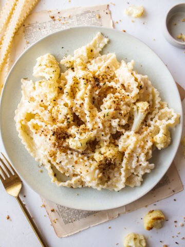 Creamy pasta with roasted cauliflower tossed in a parmesan sauce topped with toasted panko breadcrumbs on a plate.