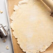 Galette pastry dough rolled out into an oval shape on a piece of parchment on a baking sheet with dusted flour and a rolling pin.