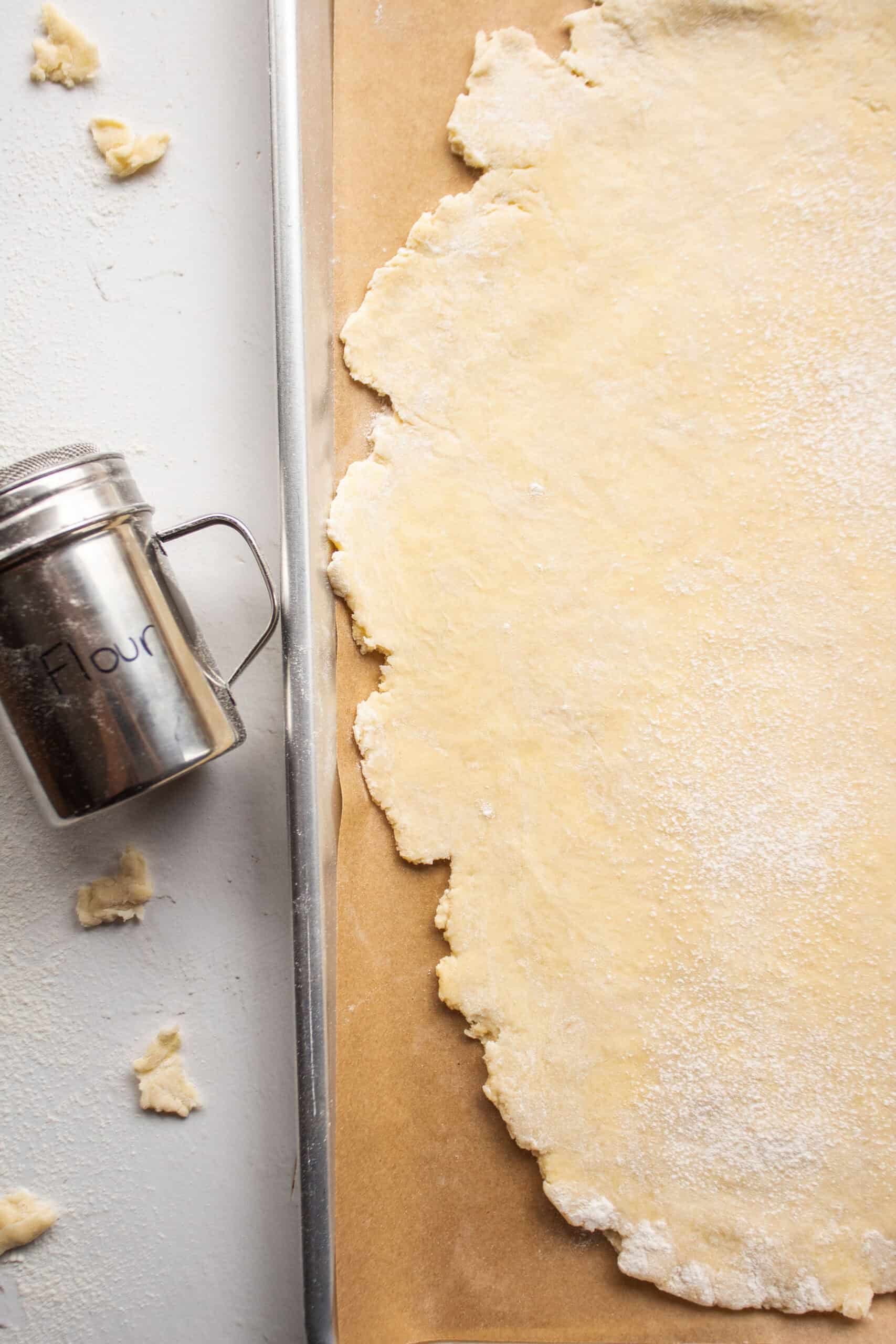 Galette pastry dough rolled out into an oval shape on a piece of parchment on a baking sheet.