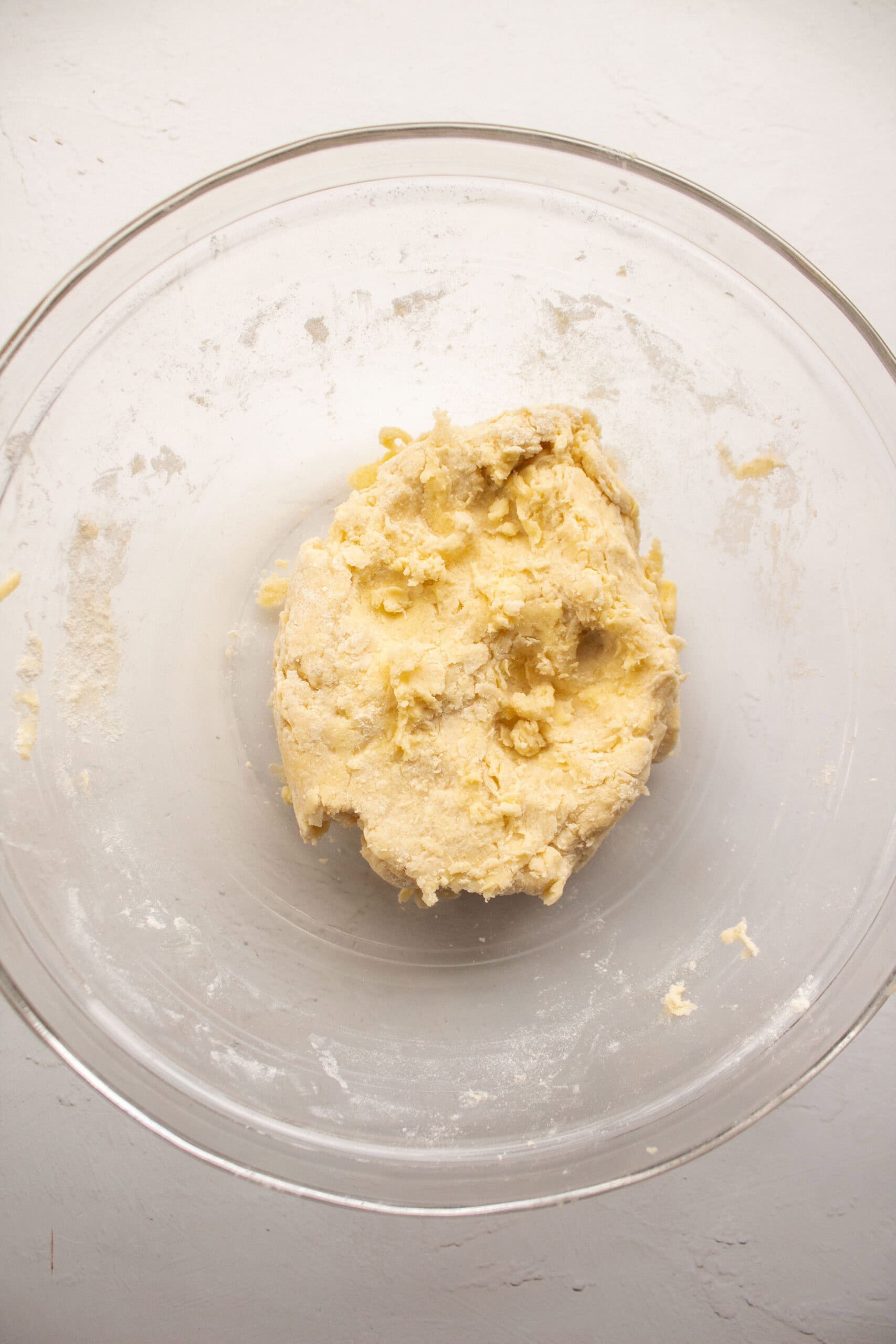 Ice cold water added to a bowl of mixed butter, flour, sugar, and salt, then kneaded together into a ball of dough.