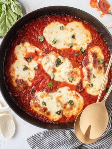 Skillet chicken parmesan in a cast iron skillet with two gold serving utensils laying on top.