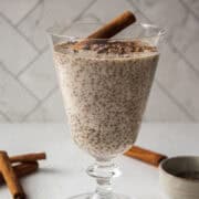 Cinnamon chia seed pudding with a scoop of Multi Collagen Advanced Lean in a glass topped with cacao nibs and a cinnamon stick on a white board.