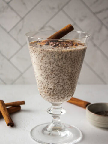 Cinnamon chia seed pudding with a scoop of Multi Collagen Advanced Lean in a glass topped with cacao nibs and a cinnamon stick on a white board.