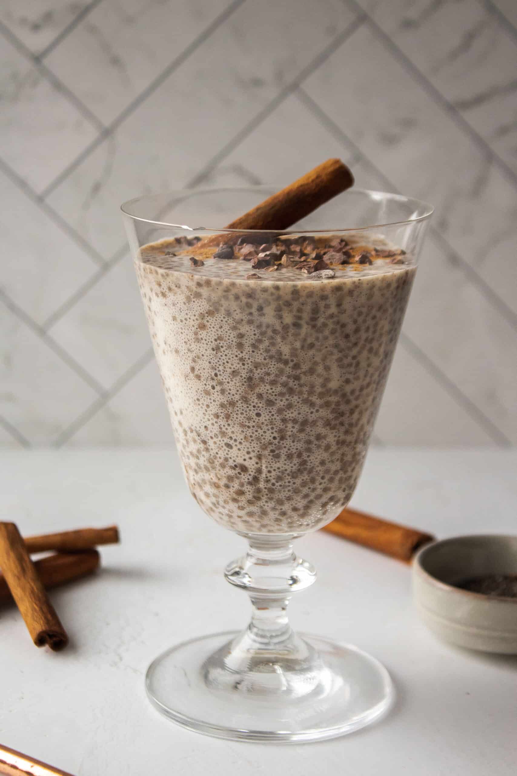 Cinnamon chia seed pudding with a scoop of Multi Collagen Advanced Lean in a glass topped with cacao nibs and a cinnamon stick on a white board.