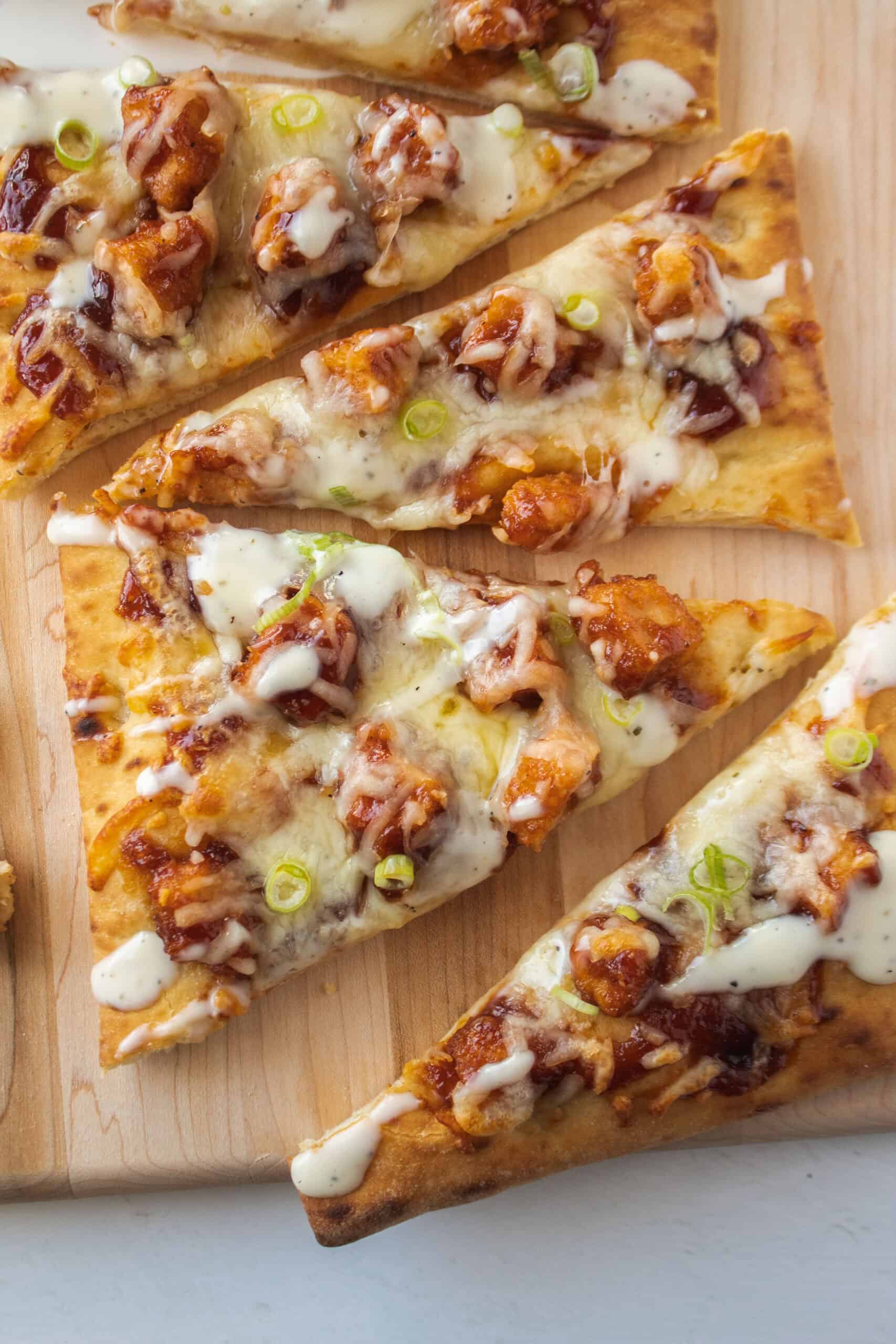 Close up of a slice of barbecue chicken flatbread on a serving board.