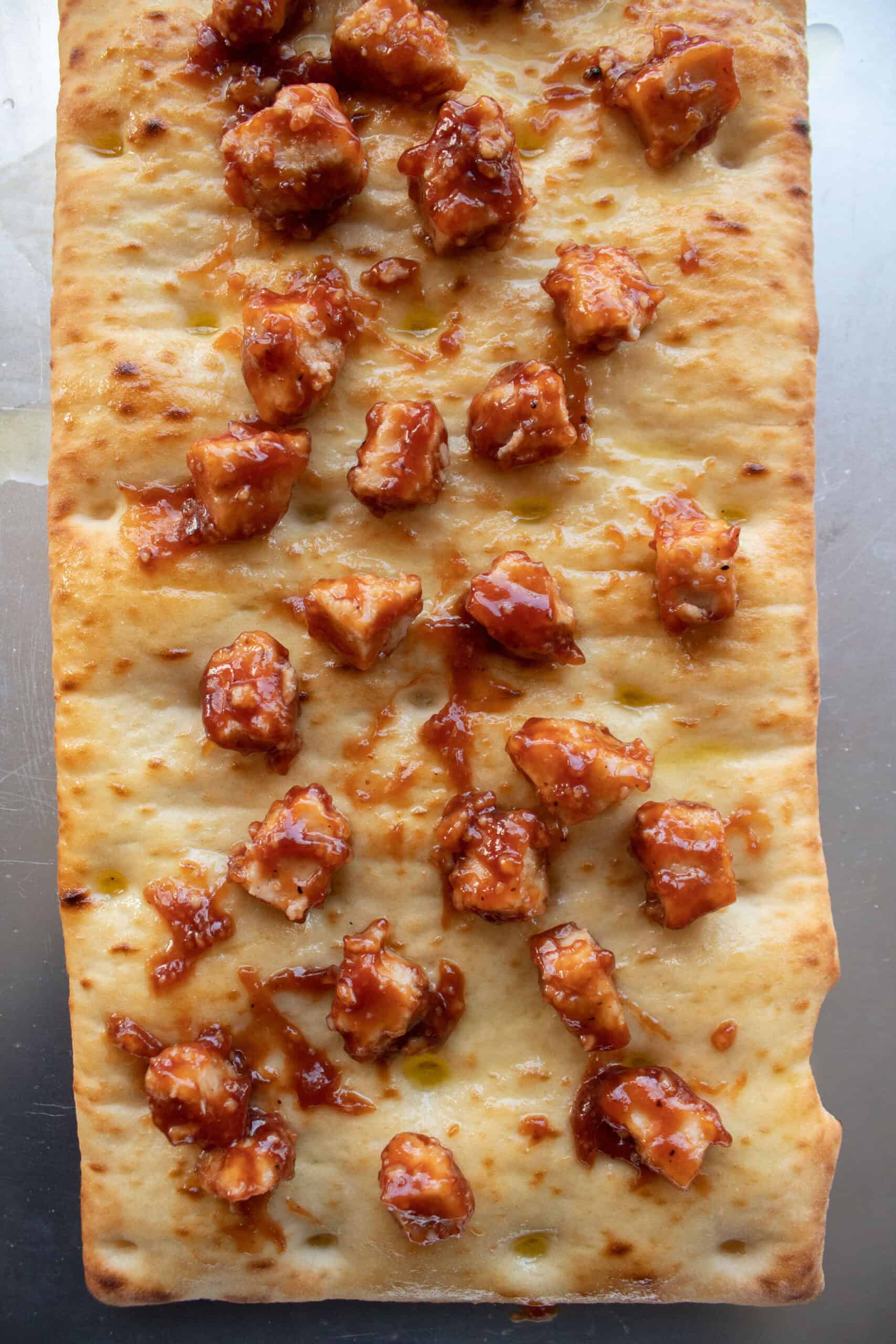 Diced pre cooked chicken nuggets tossed in barbecue sauce on top of a flatbread crust.