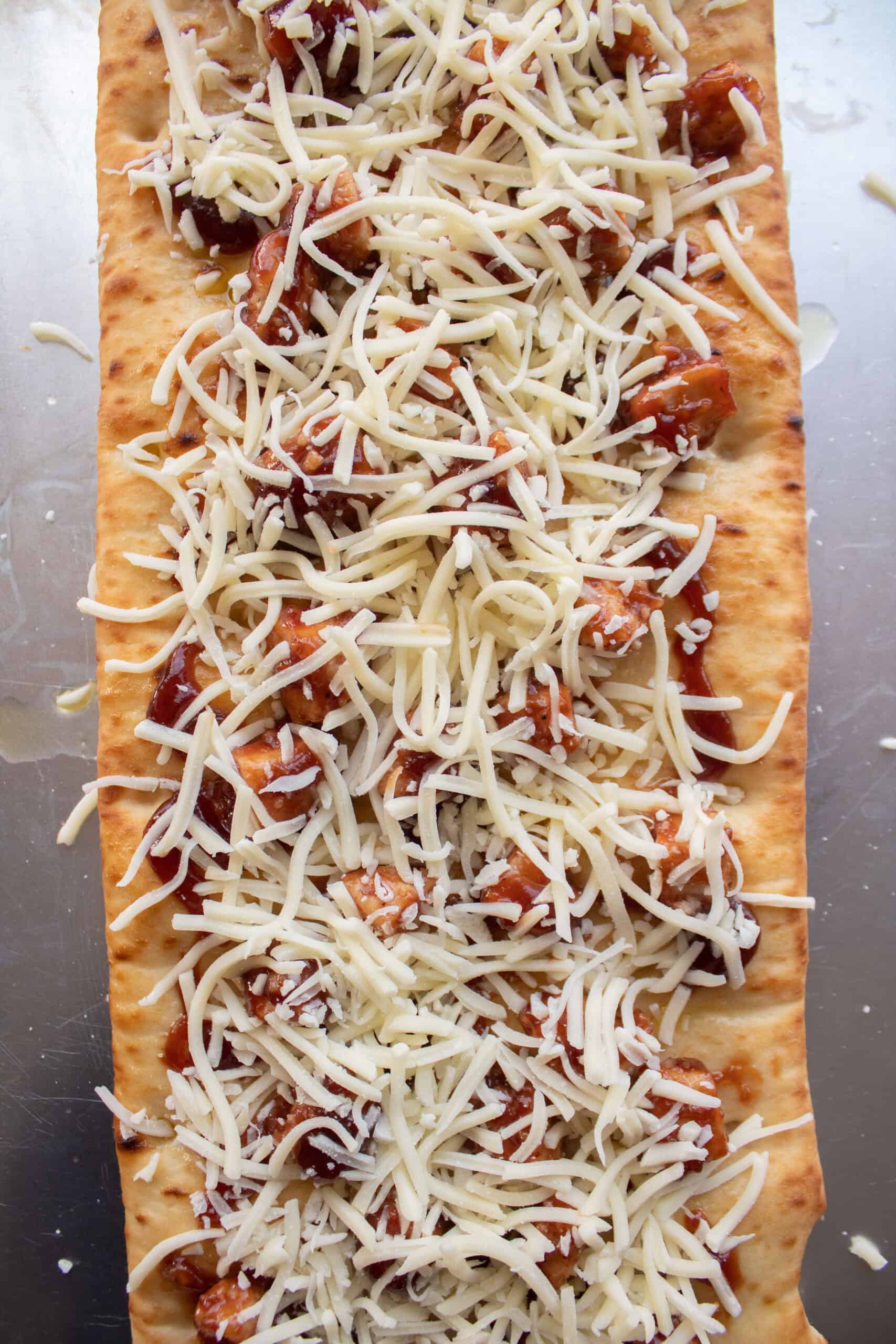Diced pre cooked chicken nuggets tossed in barbecue sauce on top of a flatbread crust with mozzarella cheese before baking.