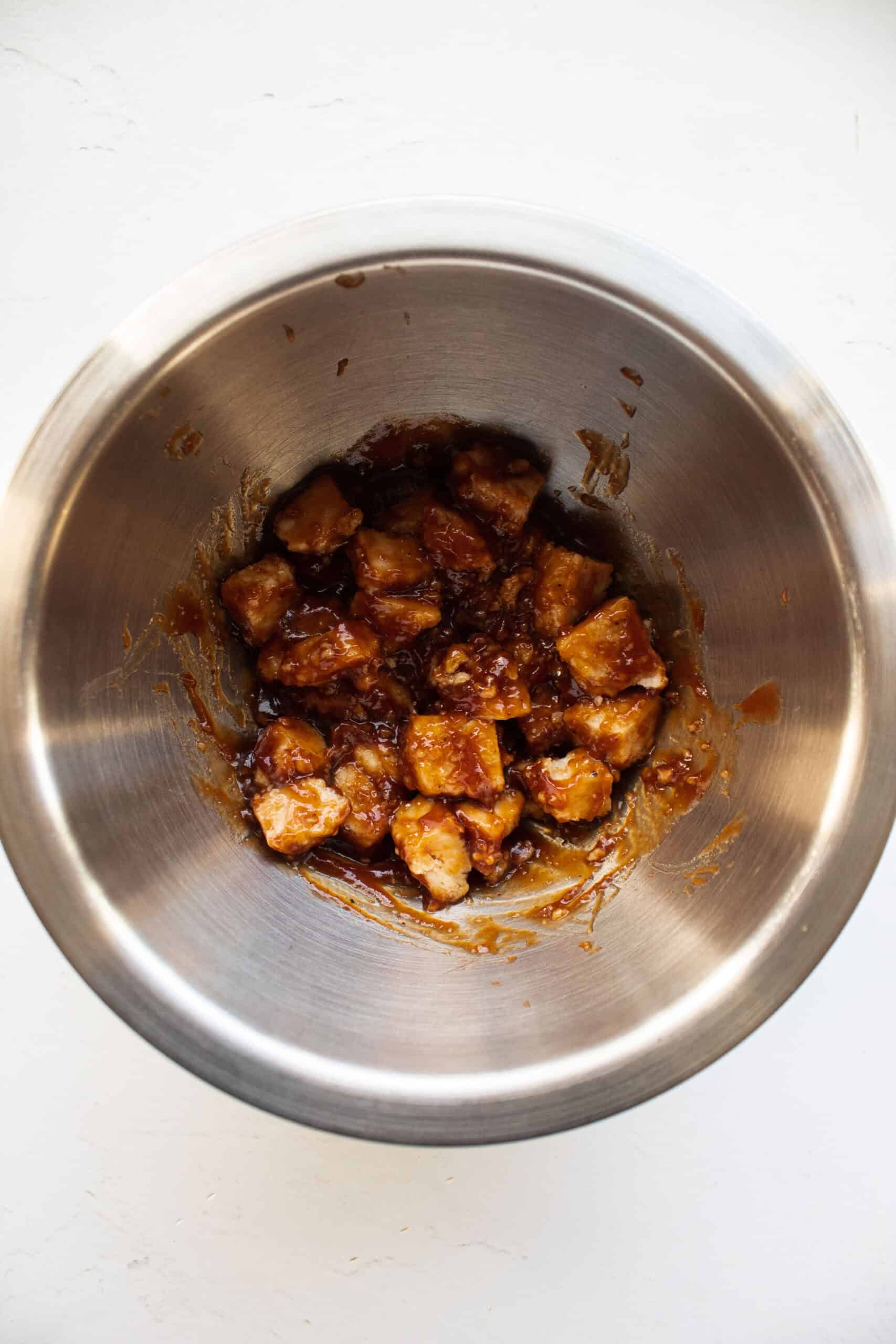 Diced pre-cooked chicken nuggets tossed in a bowl with bbq sauce.