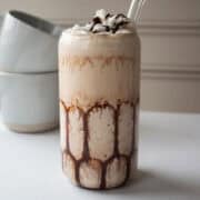High protein mudslide mocktail with a straw in it and two coffee mugs in the background.