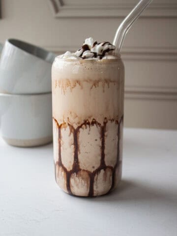 High protein mudslide mocktail with a straw in it and two coffee mugs in the background.