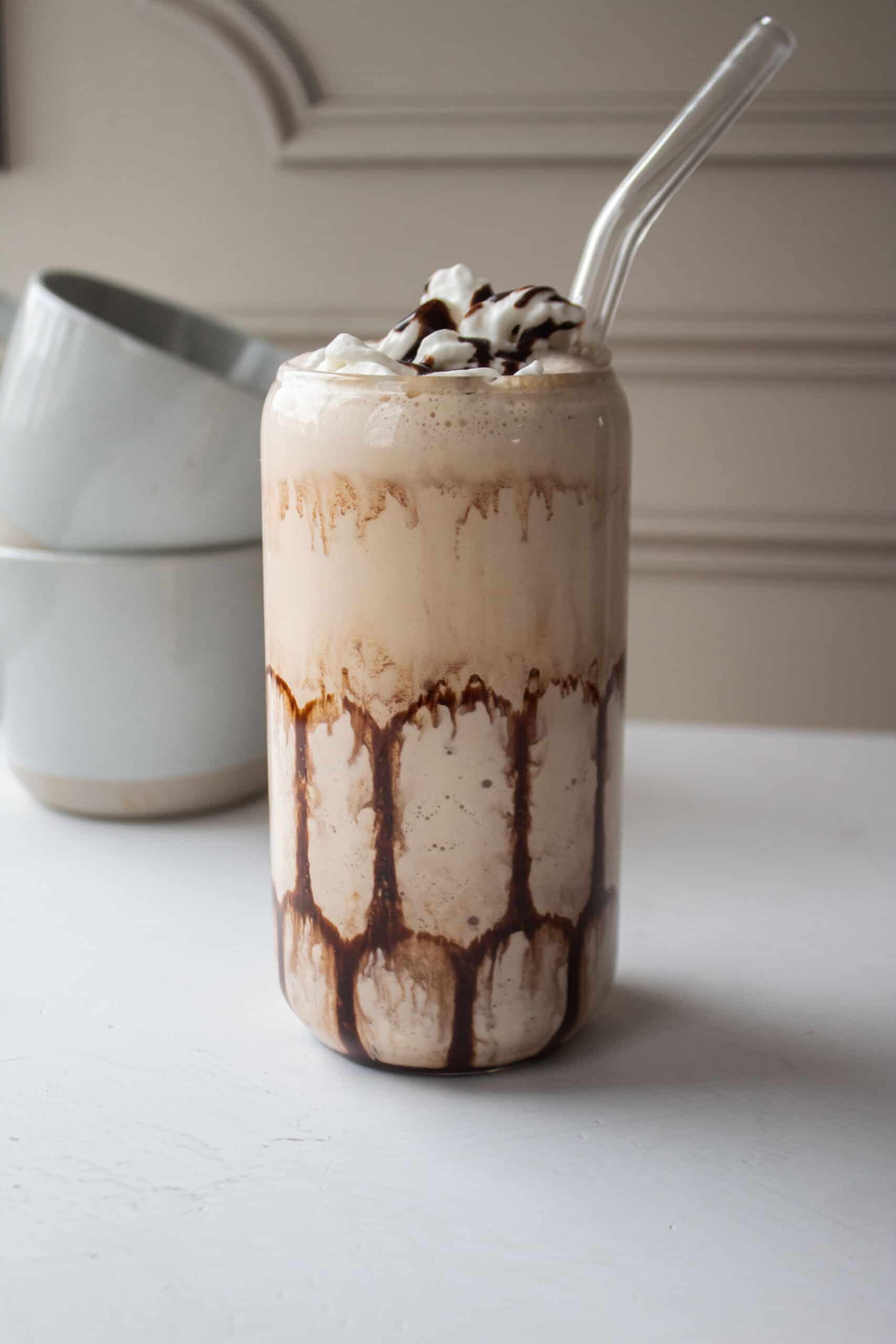 High protein mudslide mocktail with a straw in it and two coffee mugs in the background.