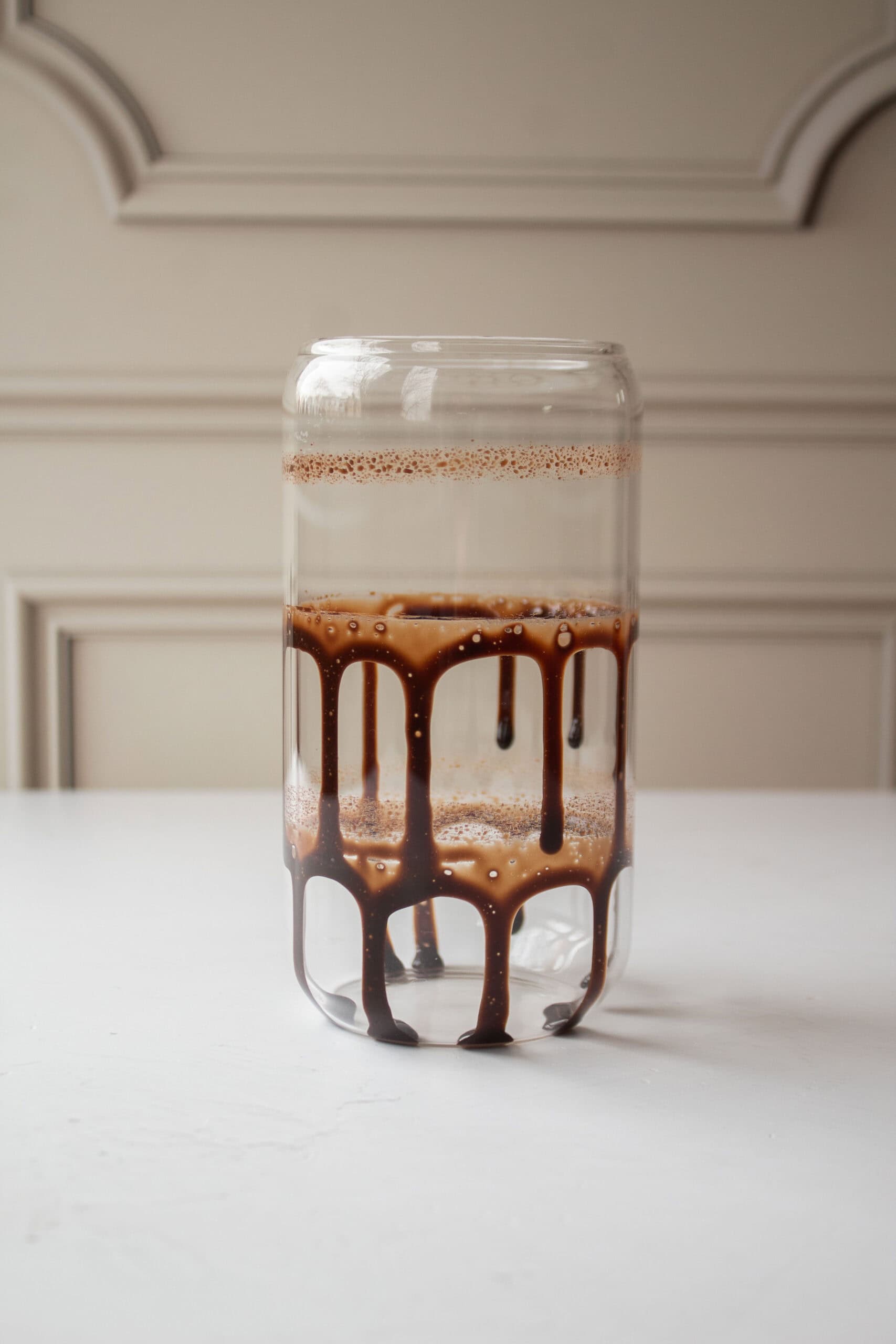 A glass with three rings of chocolate syrup on the inside of the glass dripping down the sides.