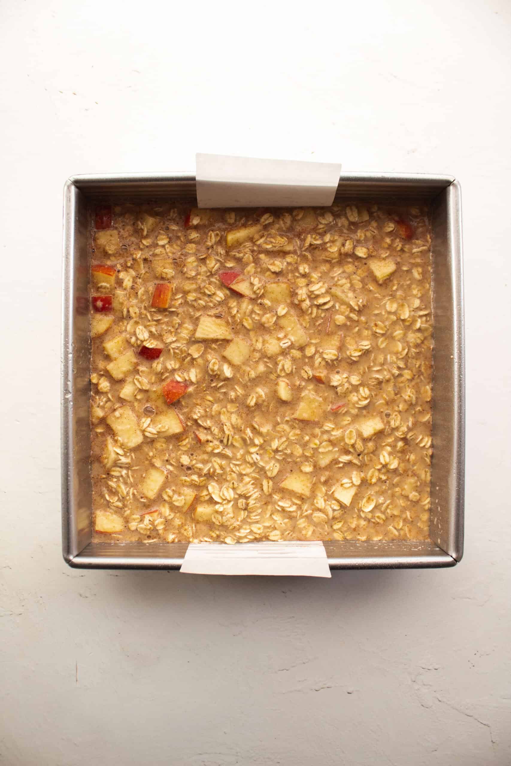 Apple cinnamon baked oatmeal in an 8x8 pan lined with parchment paper before baking.