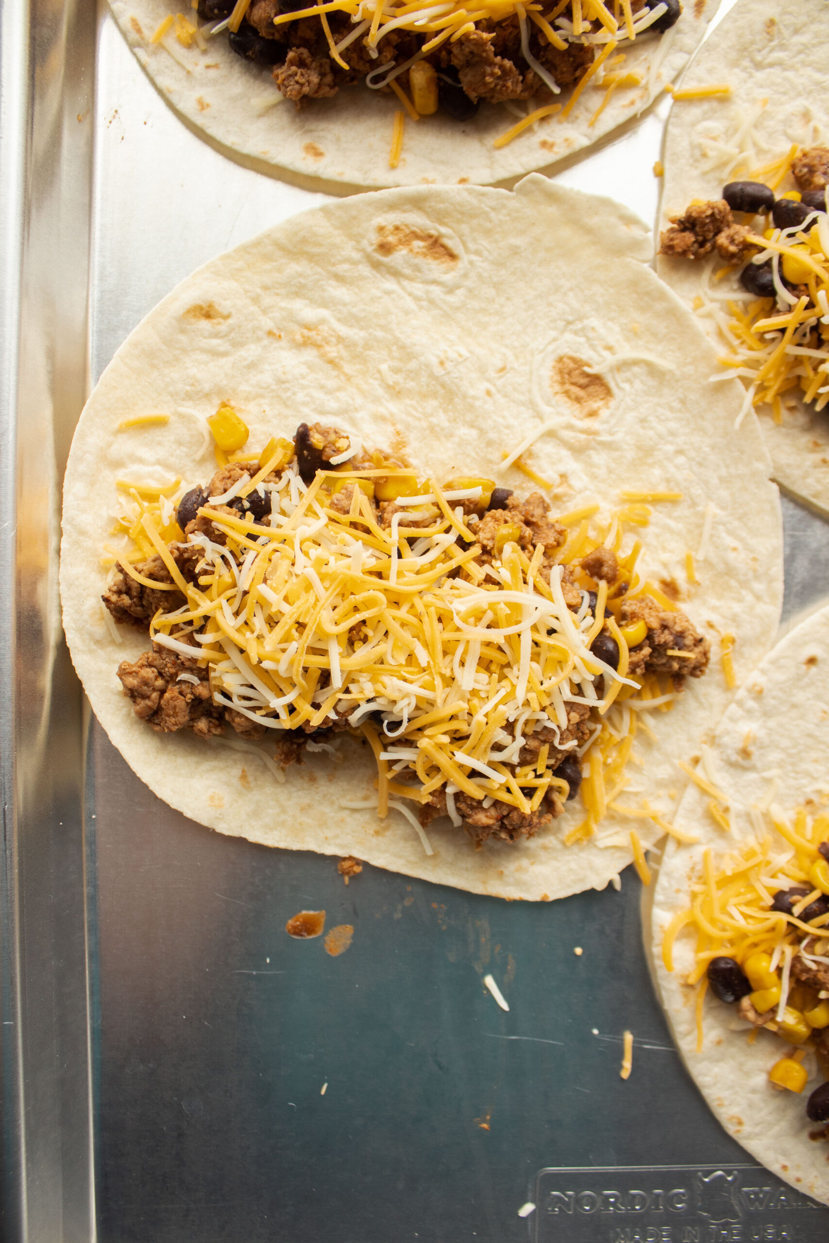 Close up of a flour tortilla filled with cheese, ground turkey, corn, black beans topped with more cheese.