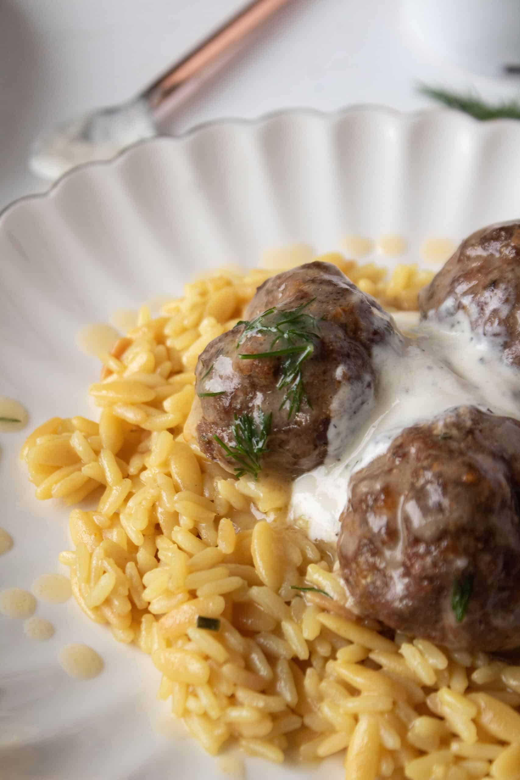 Close up of a mediterranean meatball on a plate with rice pilaf topped with dill gravy and tzatziki.