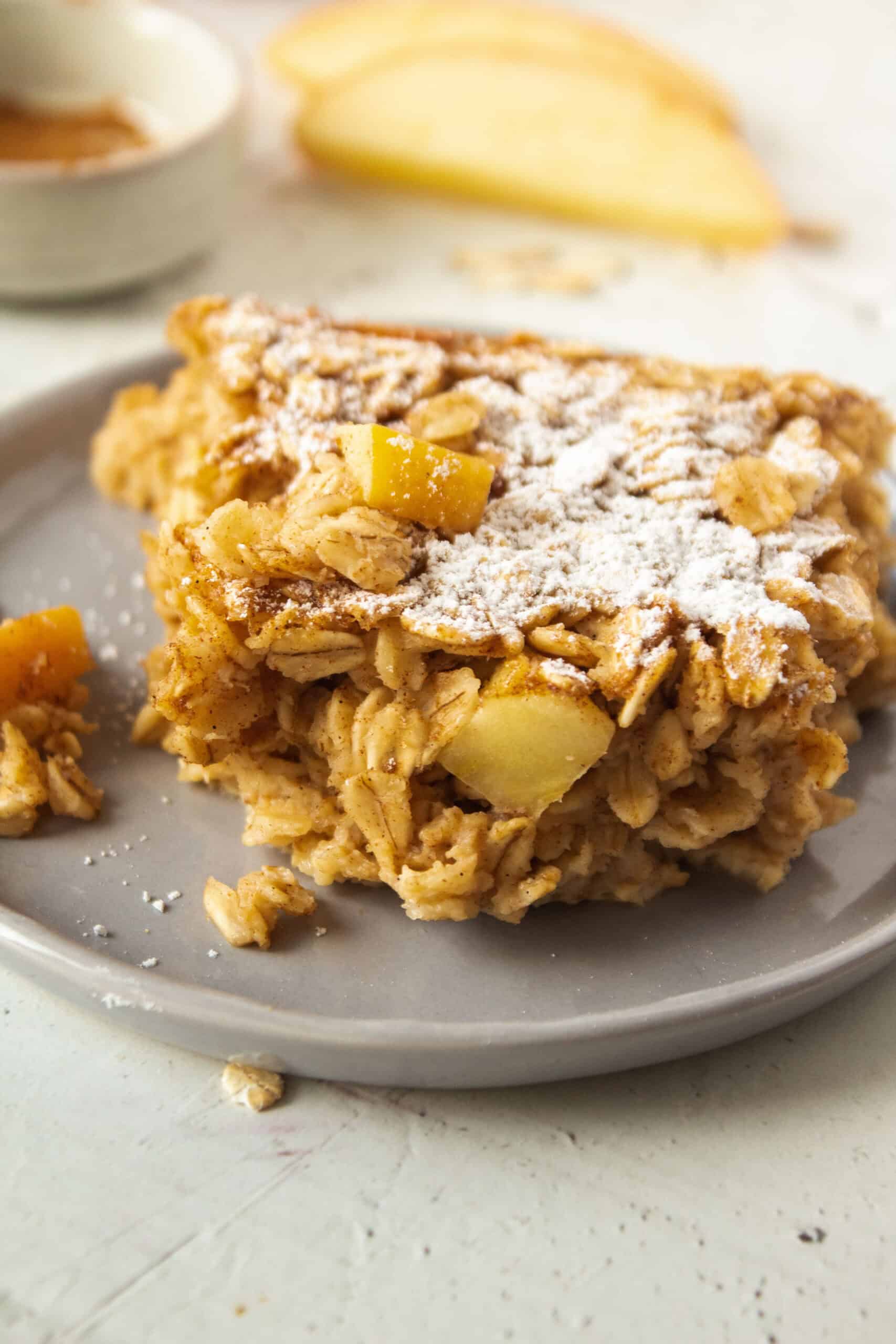 Close up of a slice of apple cinnamon baked oatmeal on a plate topped with powdered sugar.