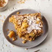 Close up of a slice of apple cinnamon baked oatmeal on a plate topped with powdered sugar.