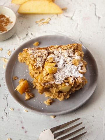 Close up of a slice of apple cinnamon baked oatmeal on a plate topped with powdered sugar.