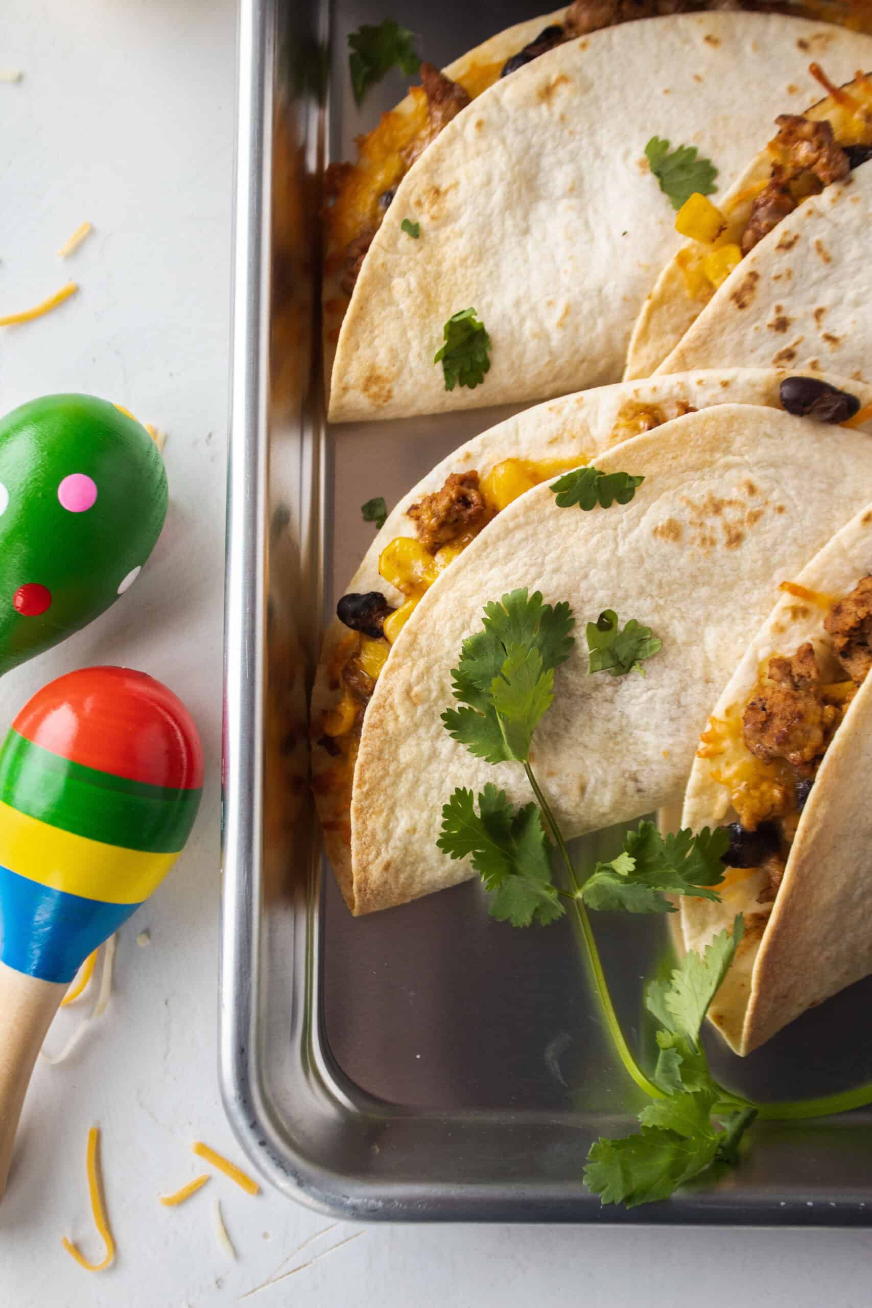 Close up of two baked ground turkey tacos on a sheet pan with maracas in the background.