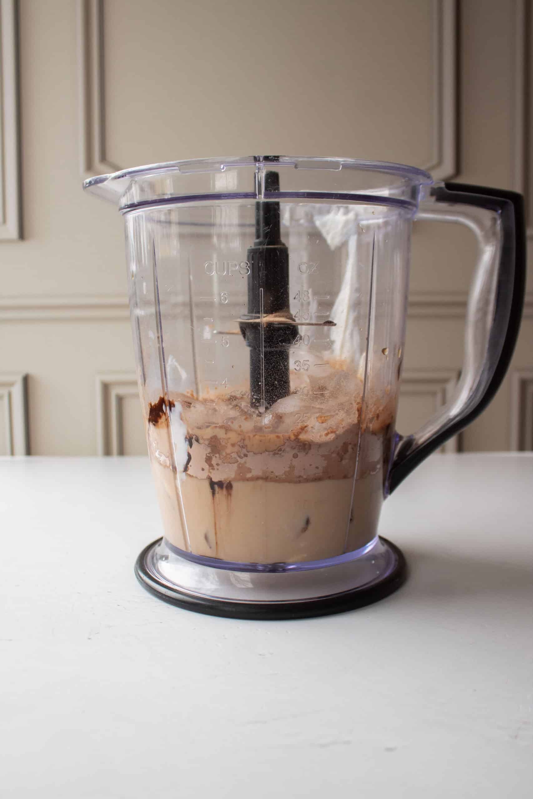 Cold coffee, milk, greek yogurt, salt, chocolate syrup, protein powder, and ice cubes in a blender.