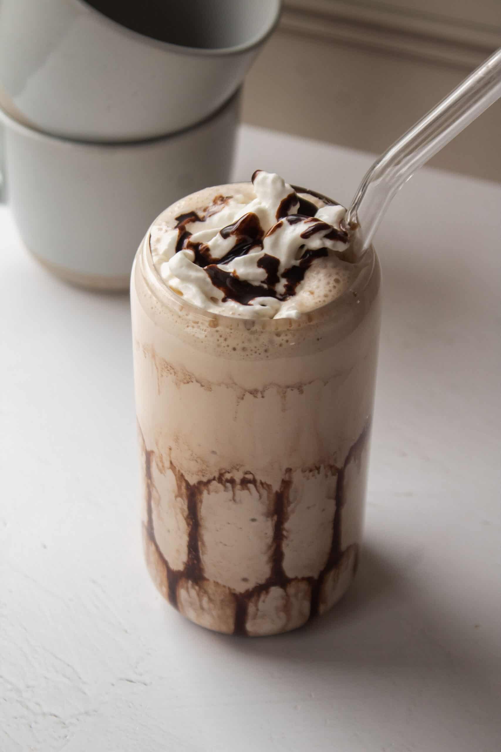 High protein mudslide mocktail with a straw in it and two coffee mugs in the background.