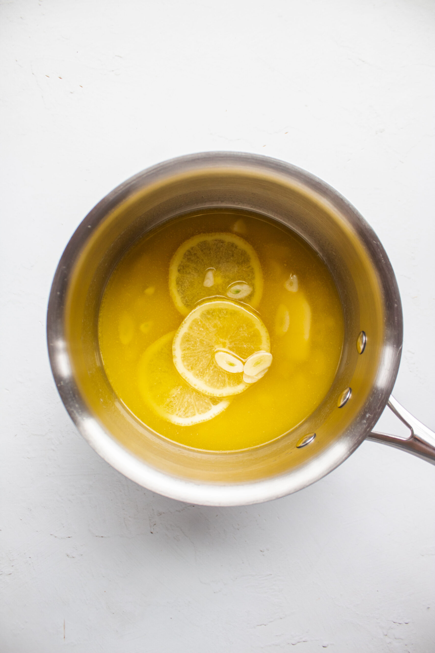 Melted butter in a saucepan with thinly sliced garlic and lemon slices.