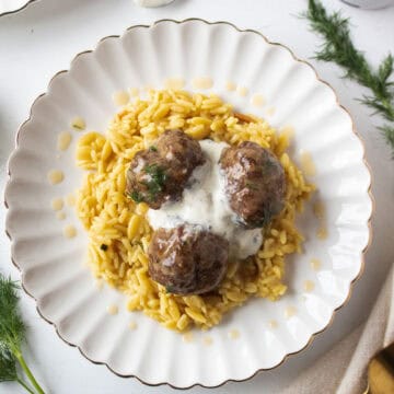Three mediterranean meatballs on a plate with rice pilaf drizzled with dill gravy and a dollop of tzatziki in the middle.