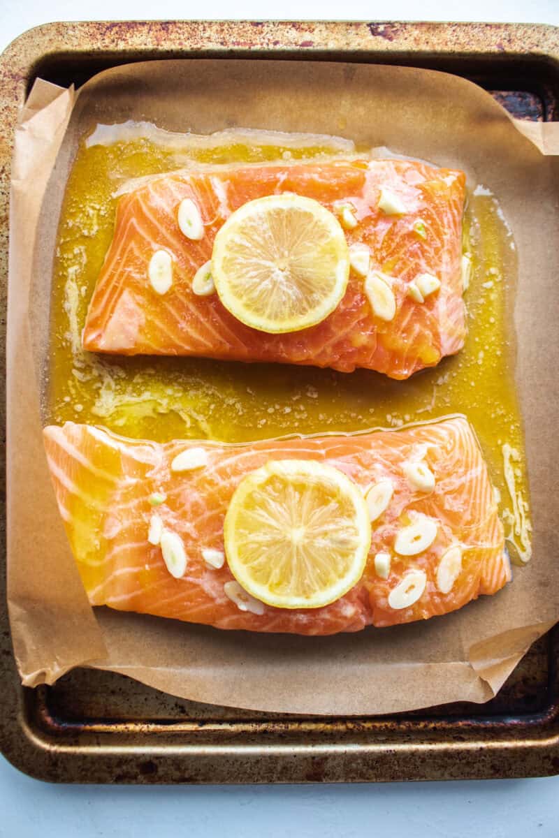 Two filets of salmon on a sheet pan topped with a lemon, butter, garlic sauce.