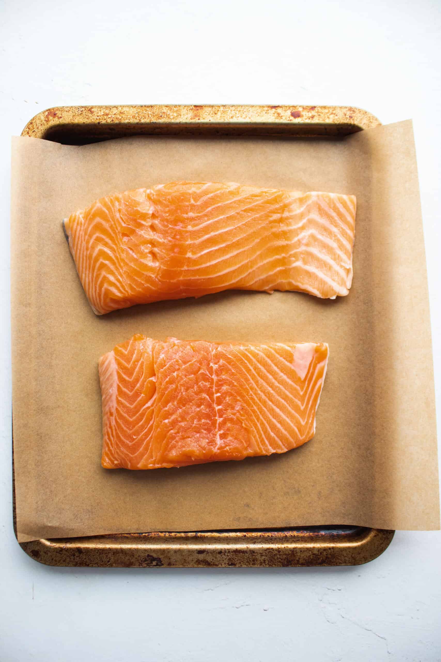 Two filets of salmon on a baking sheet with parchment paper underneath.
