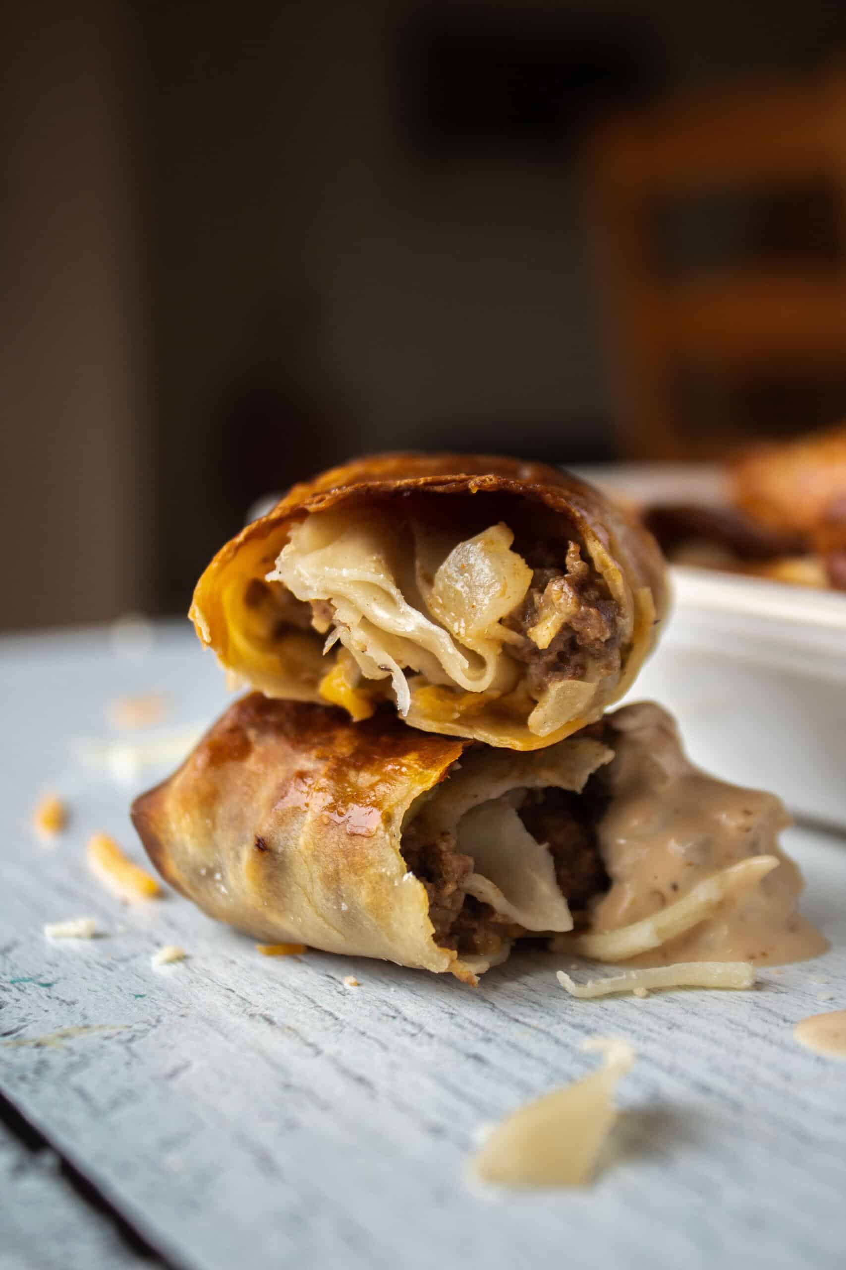 An air fryer cheeseburger egg roll ripped in half stacked on top of each other with one of the halves dipped into sauce.
