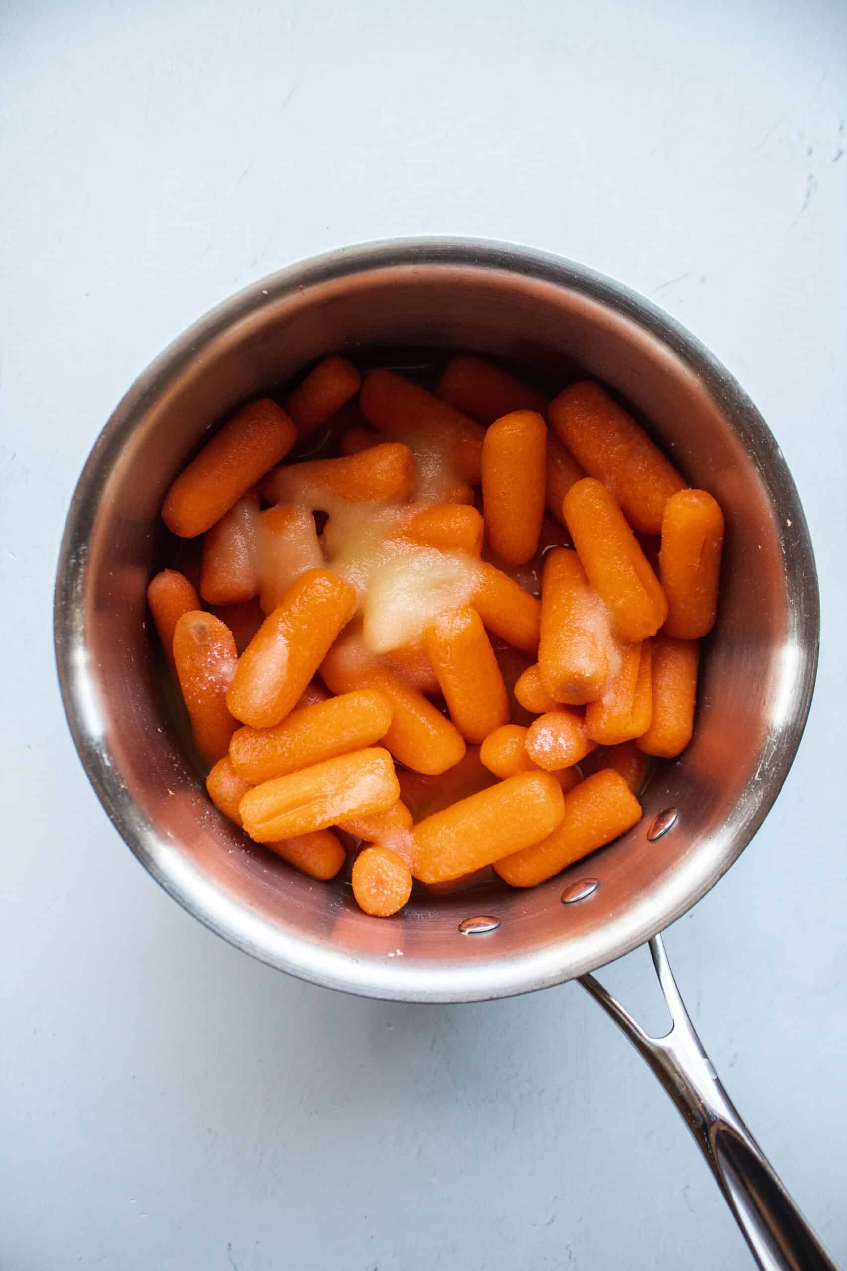 Baby carrots in a medium saucepan topped with pineapple juice and sugar.