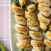Close up of a few asparagus pastry rolls on a white platter.