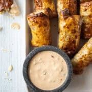 Close up of air fryer cheeseburger egg rolls on a large platter with a saucer of dipping sauce.