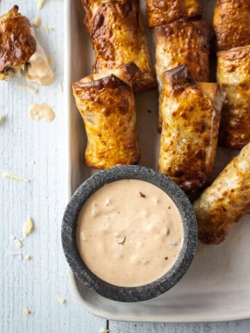 Close up of air fryer cheeseburger egg rolls on a large platter with a saucer of dipping sauce.