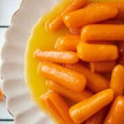 Close up of candied carrots on a small scalloped white plate.