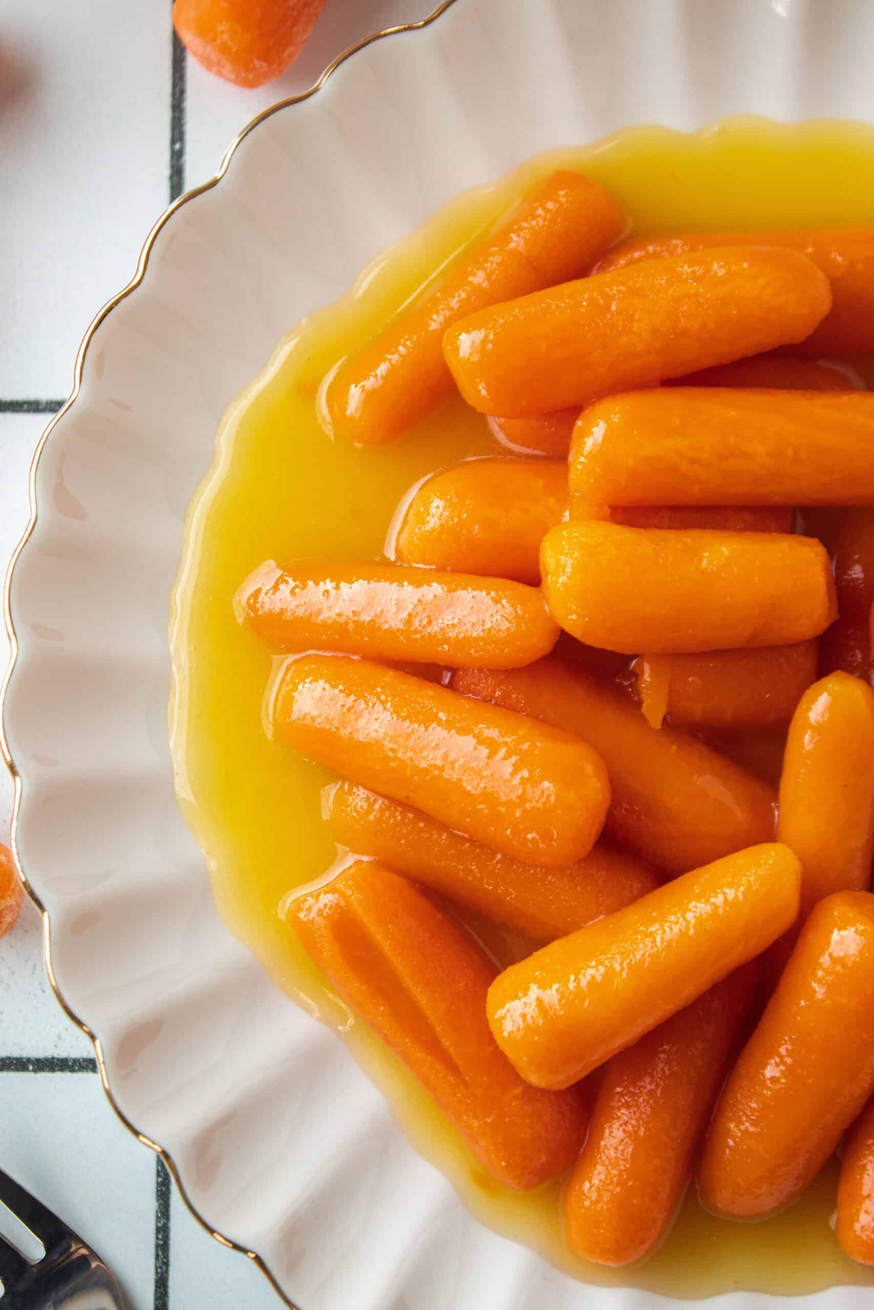 Close up of candied carrots on a small scalloped white plate.