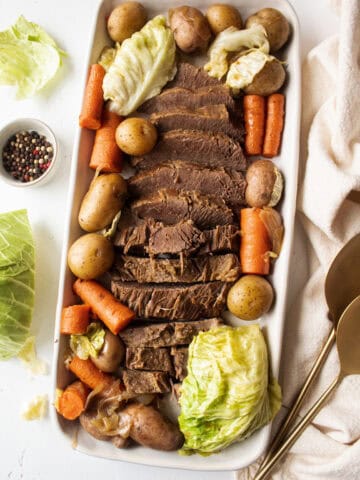 Corned beef and cabbage surrounded by cooked carrots and potatoes on a large serving platter.