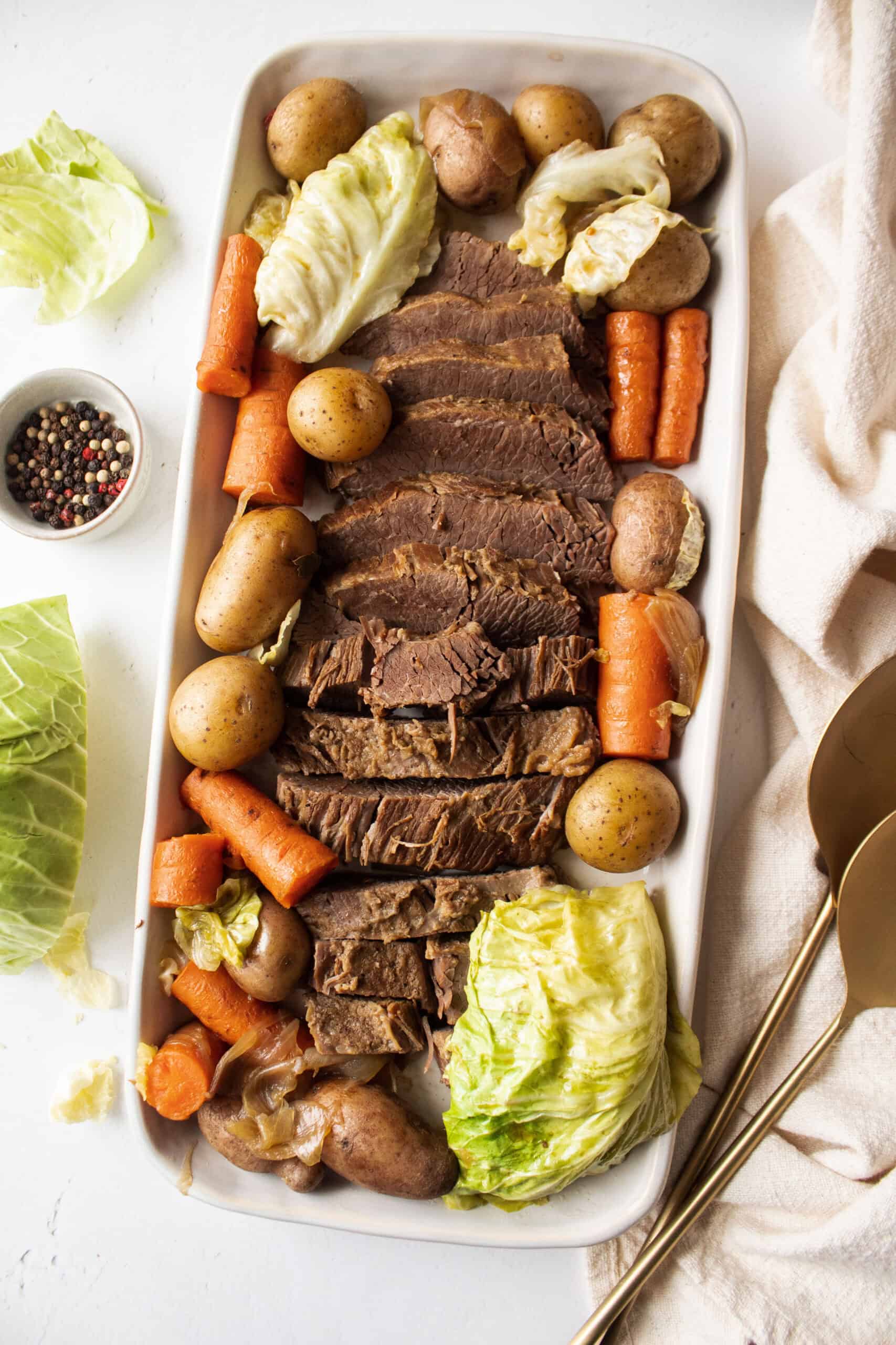 Corned beef and cabbage surrounded by cooked carrots and potatoes on a large serving platter.