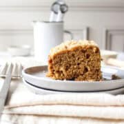A slice of a banana crumb cake topped with a streusel topping on a plate next to a fork with a napkin under it.