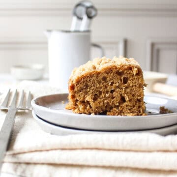 A slice of a banana crumb cake topped with a streusel topping on a plate next to a fork with a napkin under it.