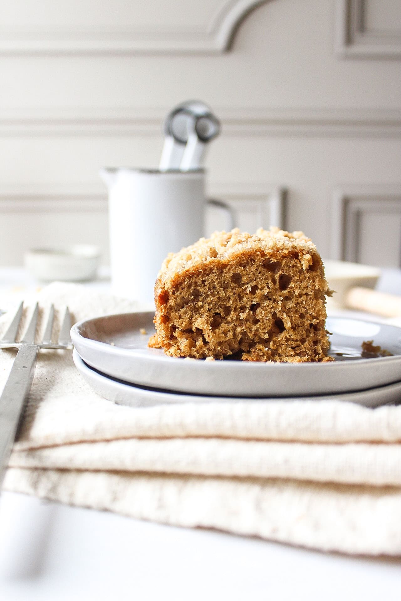 A slice of a banana crumb cake topped with a streusel topping on a plate next to a fork with a napkin under it.