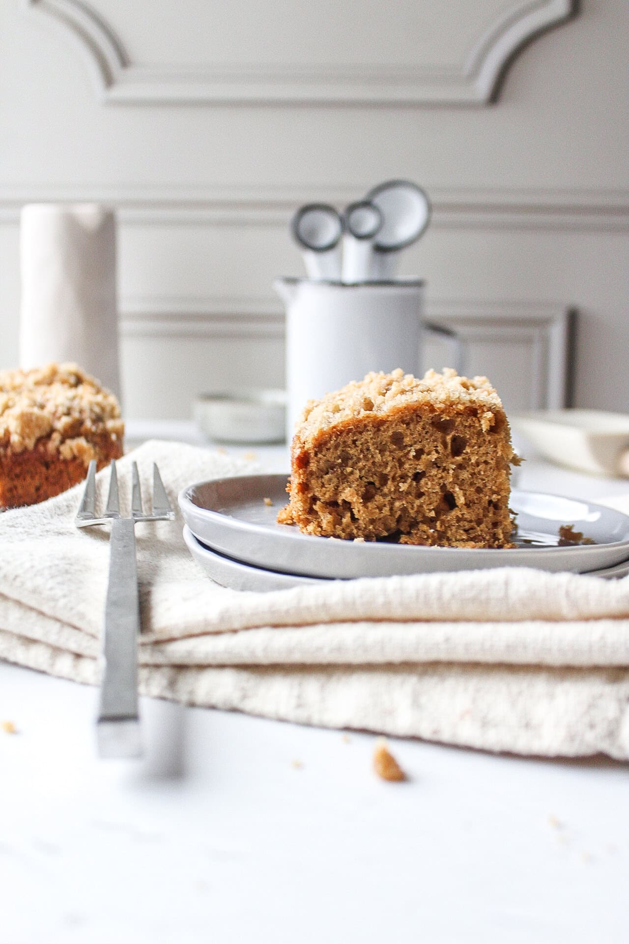 A slice of a banana crumb cake topped with a streusel topping on a plate next to a fork with a napkin under it.