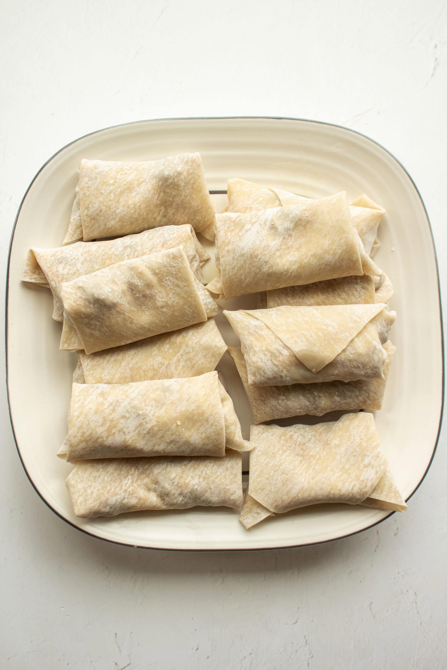 Several cheeseburger egg rolls stacked on top of each other before being air fryed.