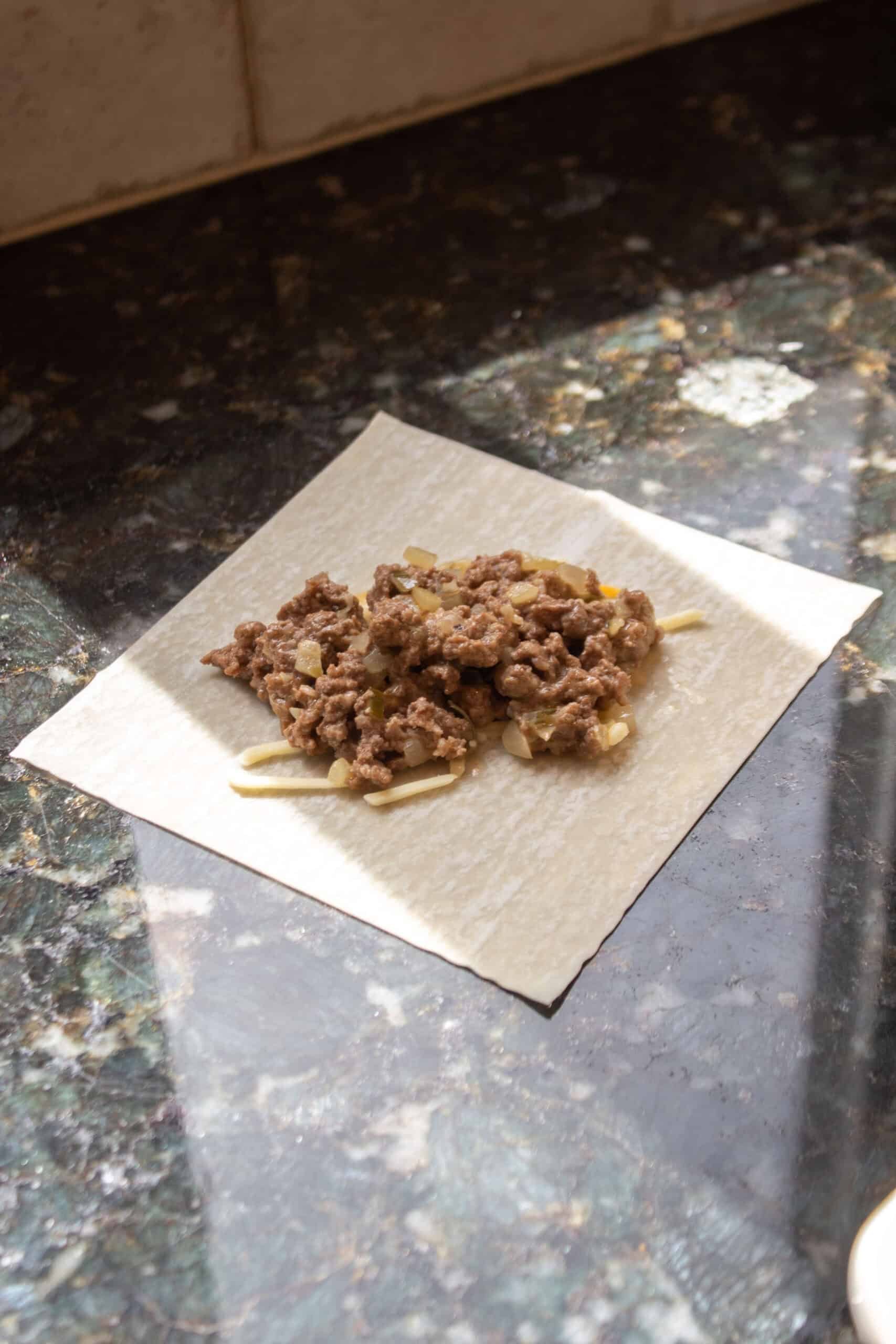 A wonton wrapper with a scoop of cheeseburger meat in the middle.